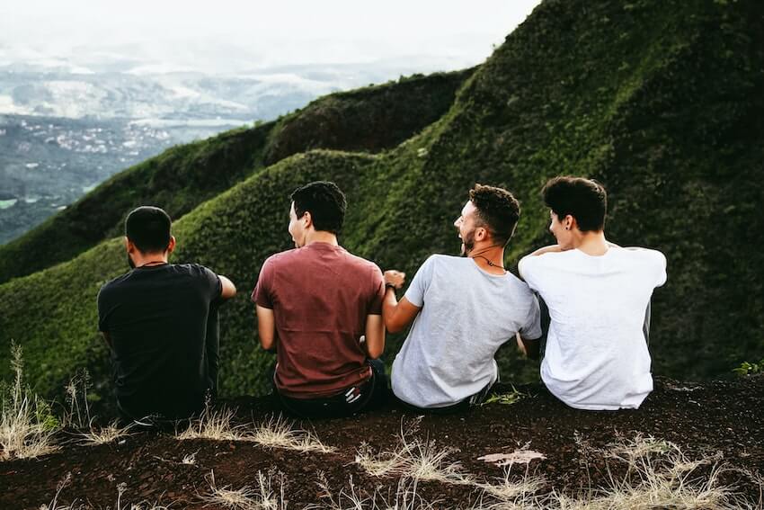 4 male friends sitting next to each other outside and having a good time