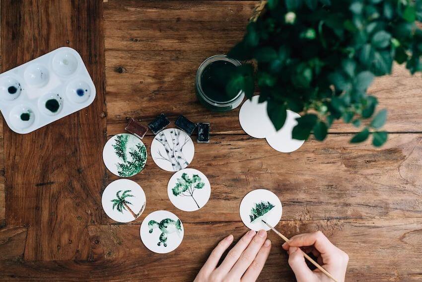 person painting pictures of plants on circular coasters