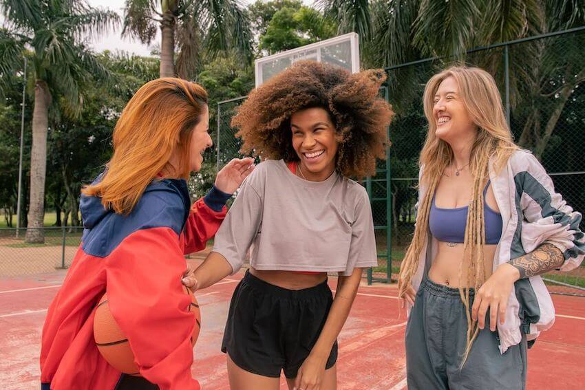 3 women standing on a basketball court laughing during a funny conversation