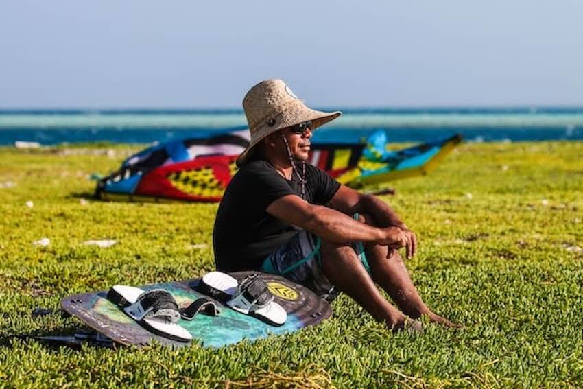man sitting on the ground next to his surfboard on a sunny day