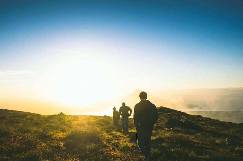 people hiking up a mountain path during sunset