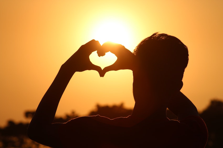 man facing the sun, making a heart with his hands