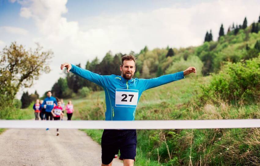 runner crossing the finish line with his arms up in celebration