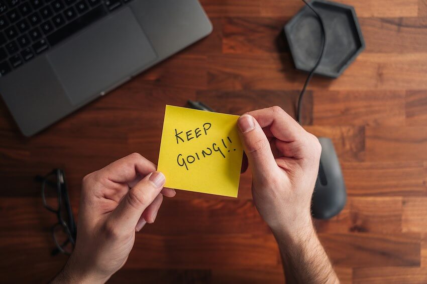 man holding a yellow sticky note that says to keep going