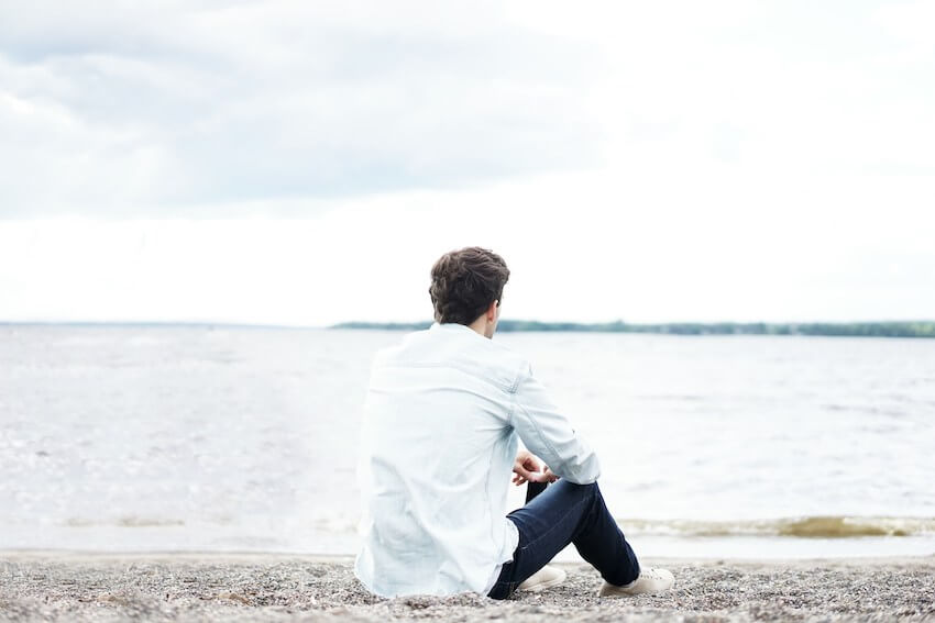 man sitting on the beach looking at the lake