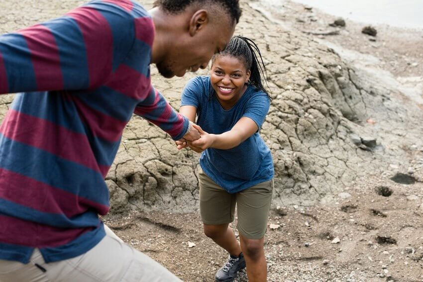 smiling man helping a smiling woman climb up