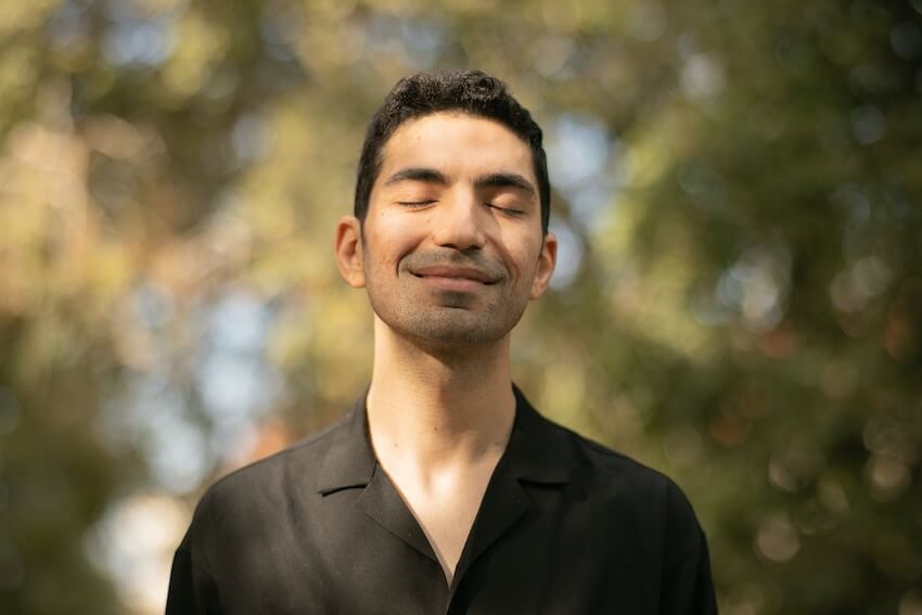 smiling man with his eyes closed, feeling the warmth of sunshine on his face