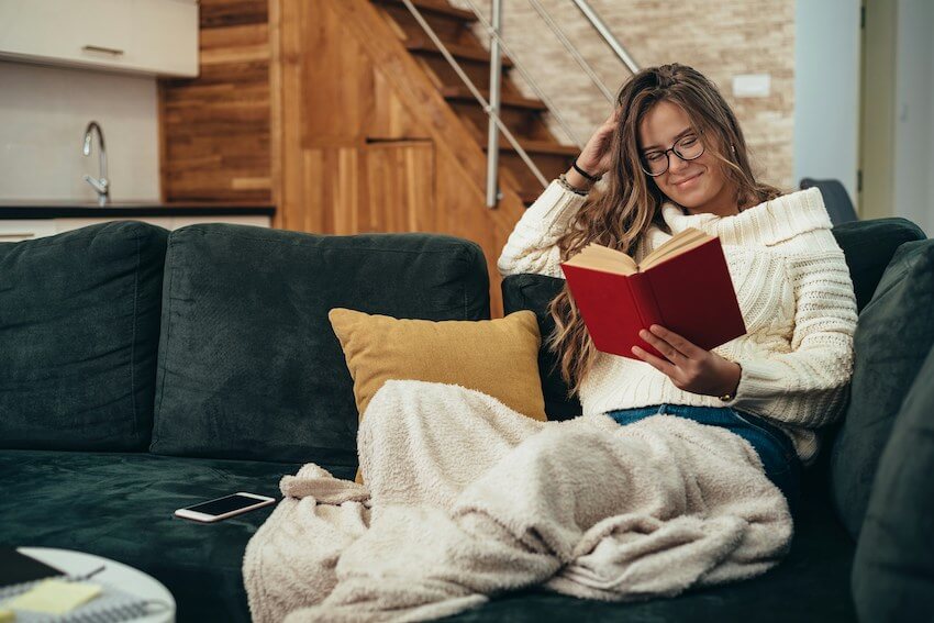 smiling woman cozy on the couch, reading a book