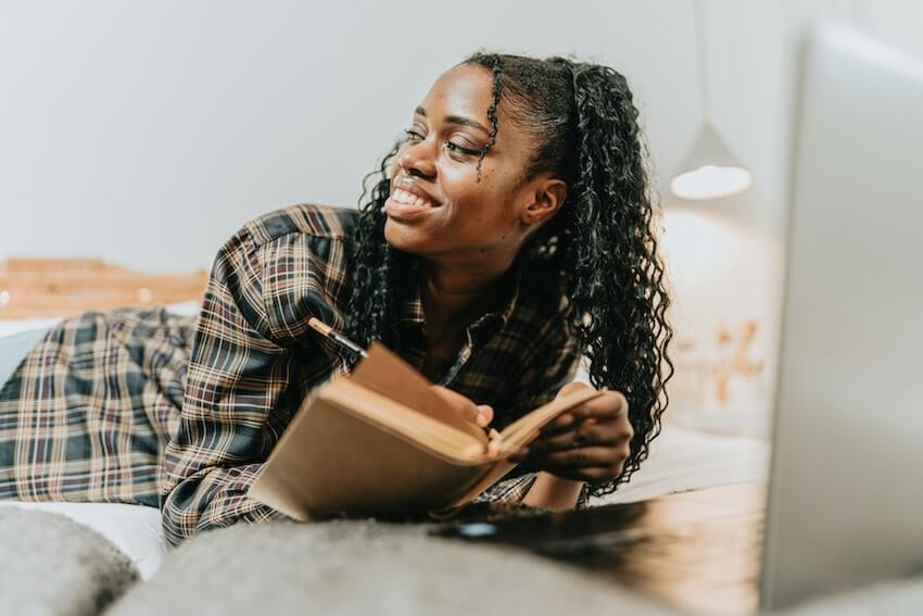 smiling woman laying in bed, journaling