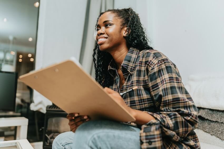 smiling woman looking up from her writing and thinking positive thoughts