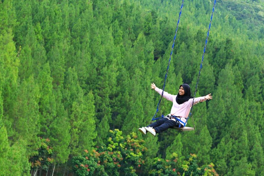smiling woman on a swing with her arms out