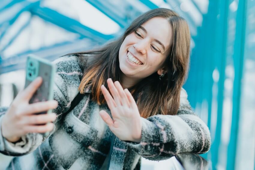 smiling woman waving at her friend on video