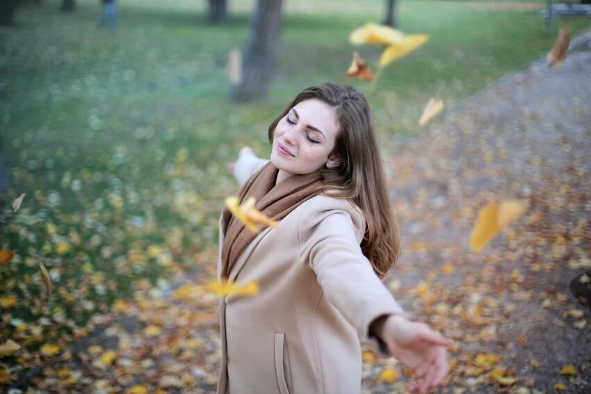 smiling woman with her arms out as autumn leaves fall around her