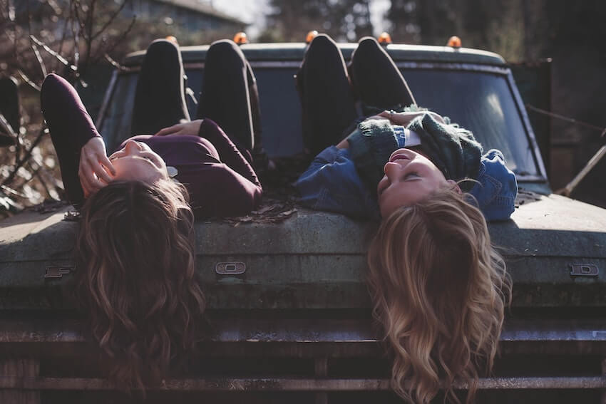 two female friends talking while laying on top of a truck