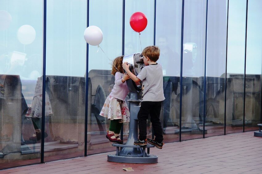 two playful kids looking at each other through a telescope