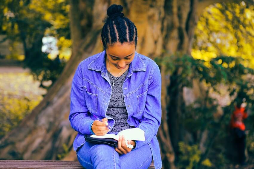 woman in denim sitting outside journaling