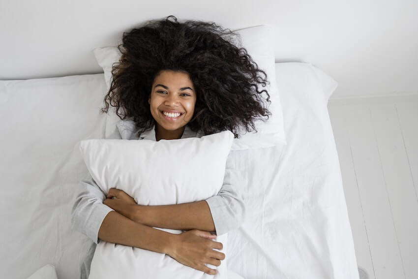 woman laying in bed, hugging her pillow, smiling