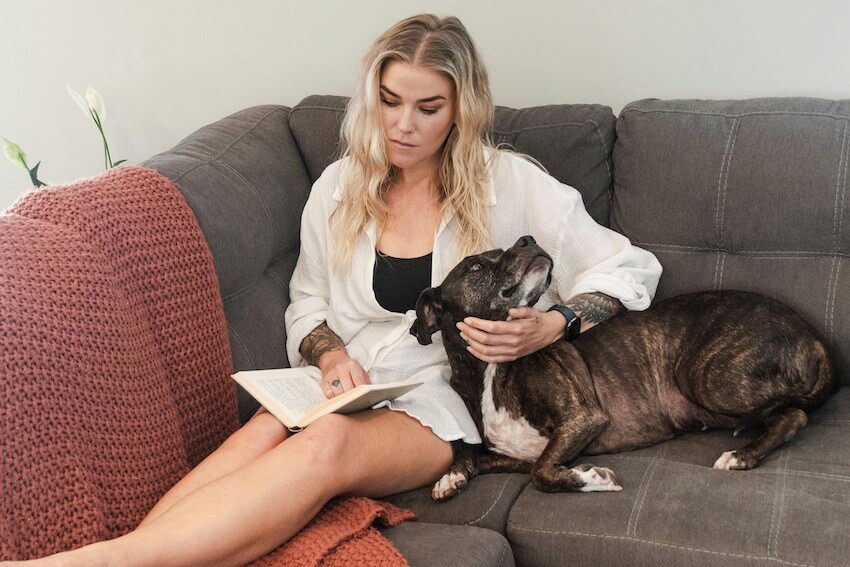 woman reading a book on the couch while petting her dog