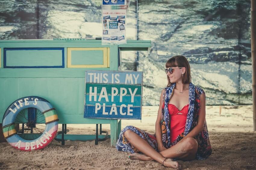 woman sitting next to a sign that reads this is my happy place