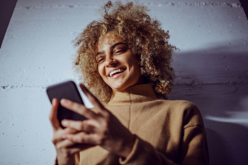 woman smiling while reading a message on her phone