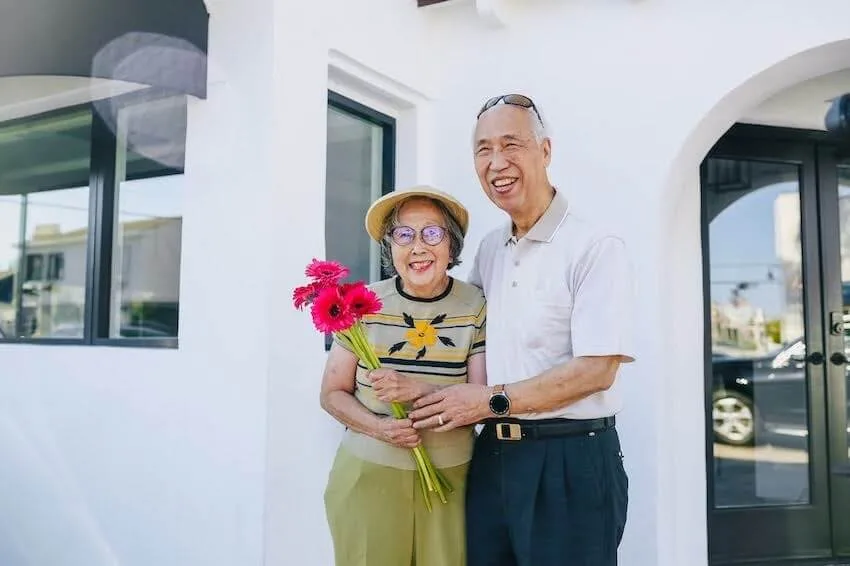 happy elderly couple smiling while holding a bouquet of pink Gerbera daisies