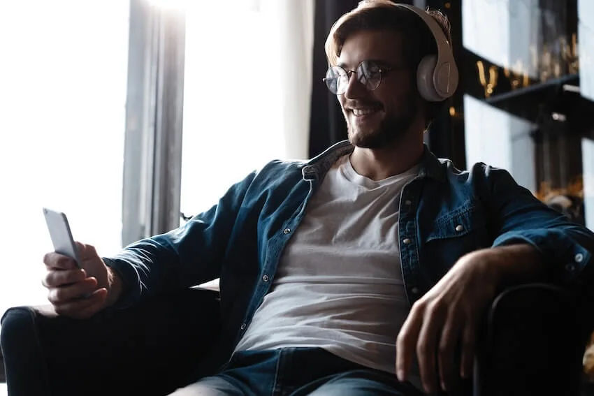smiling man wearing headphones listening to an audiobook on his phone