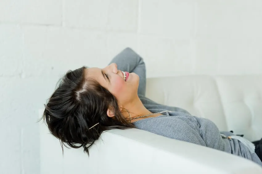 smiling woman leaning her head on the side of the couch looking up