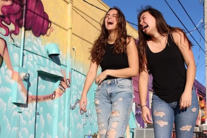 two woman laughing while walking down a street