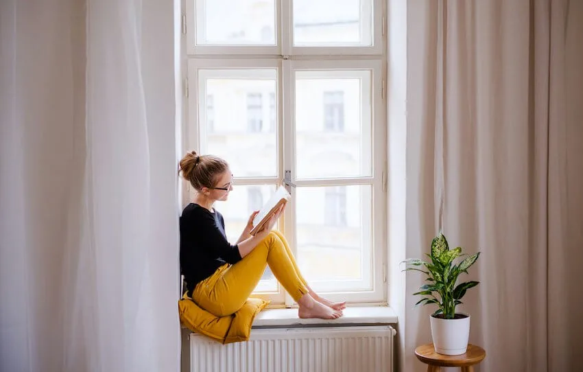 woman sitting on a windowsill reading a book