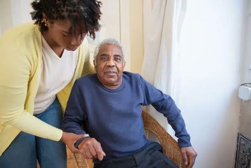 Woman helping an elderly man out of his chair