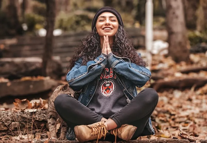 woman sitting cross legged, smiling with her eyes closed and her hands pressed together