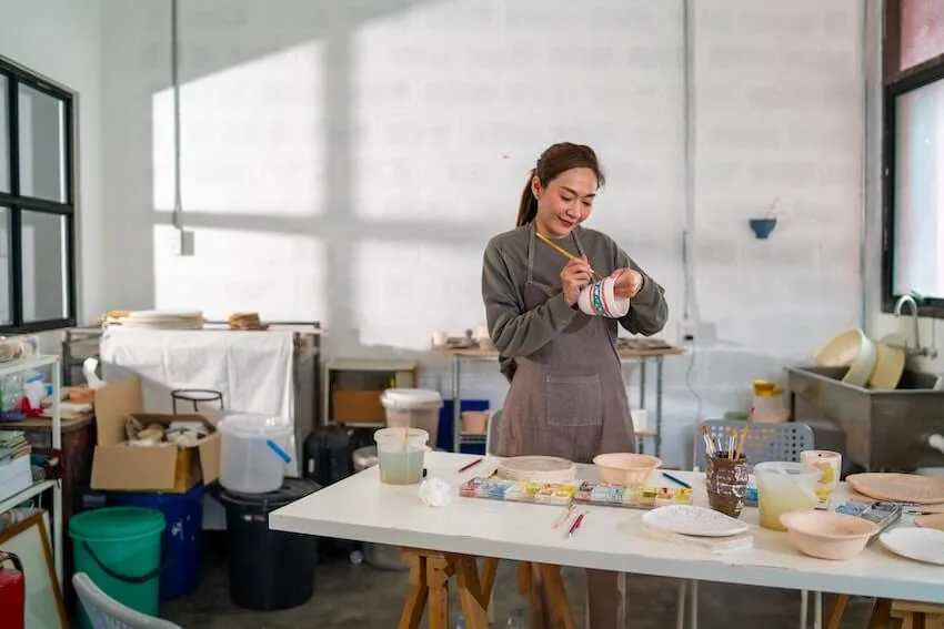 a smiling woman painting on pottery