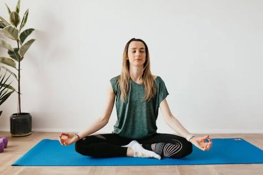 woman sitting cross legged with her eyes closed on a yoga mat