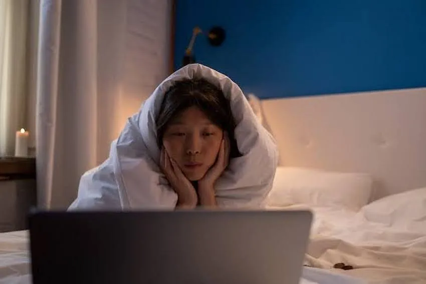 Woman wrapped in her blanket while looking at her laptop