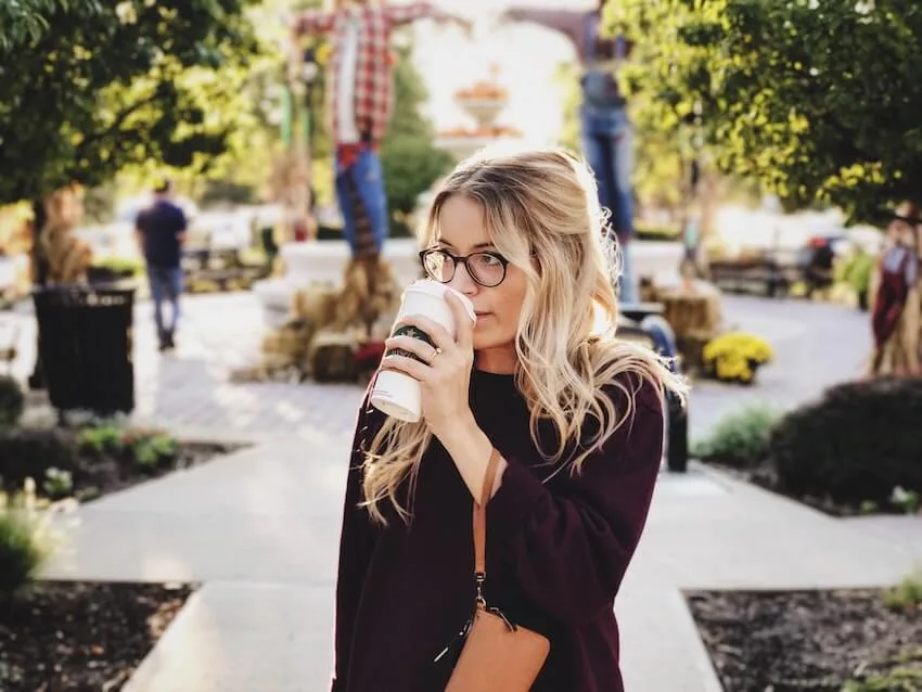 woman sipping a to-go cup of coffee as she walks in her neighborhood