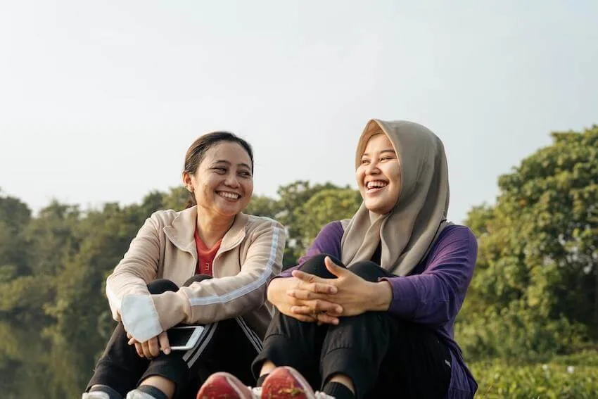 two women sitting on the ground outside laughing together