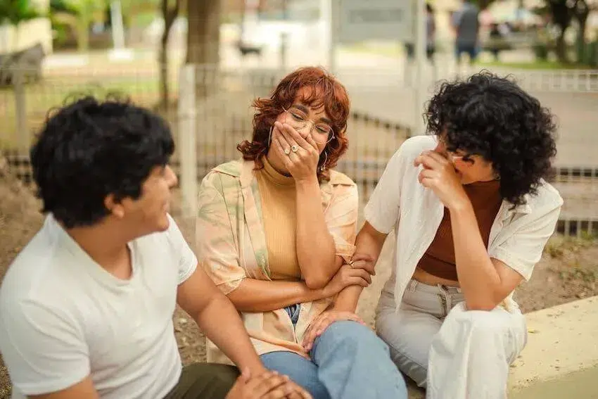 3 friends cracking jokes, one of them is covering her mouth trying not to laugh out loud