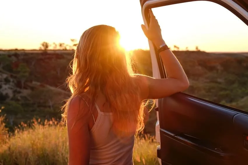 woman standing outside her car admiring the view at sunset