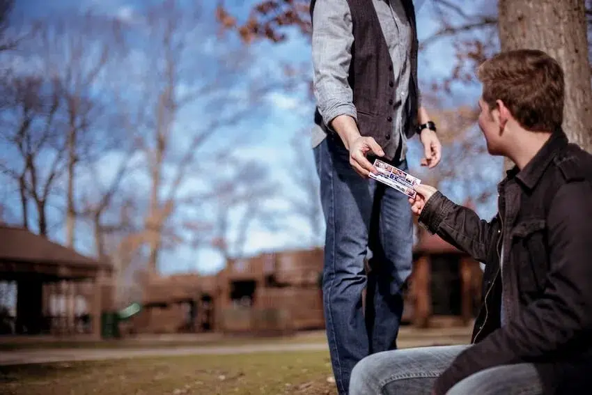 a person handing something to a man who's sitting on the ground