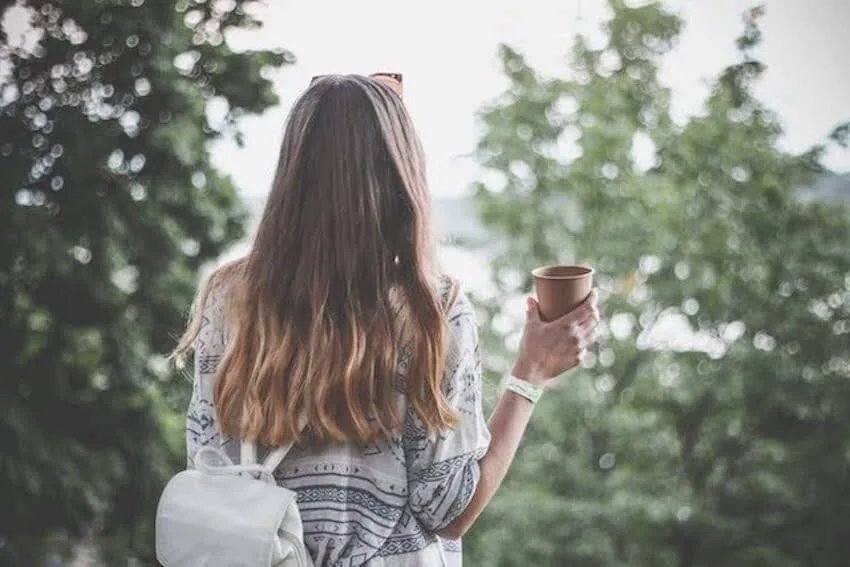 woman holding a cup while looking out into the woods