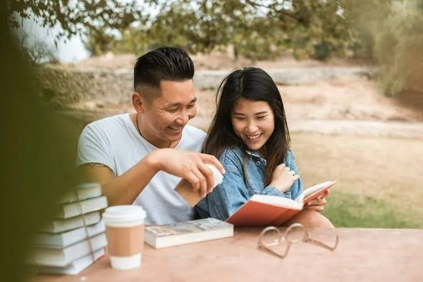a smiling couple reading a book together outside