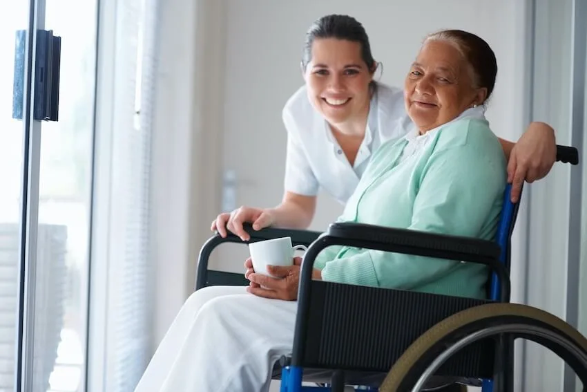 a smiling woman helping an elderly woman in a wheelchair