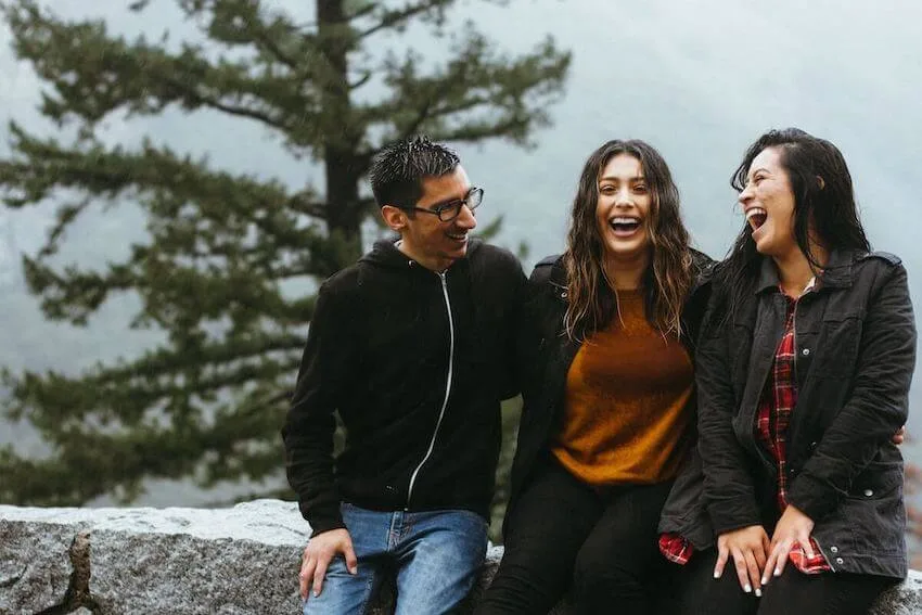 3 friends sitting outside on a ledge laughing together