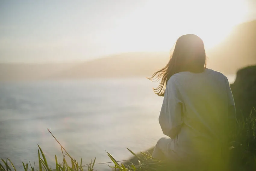 woman sitting peacefully outside looking at a body of water