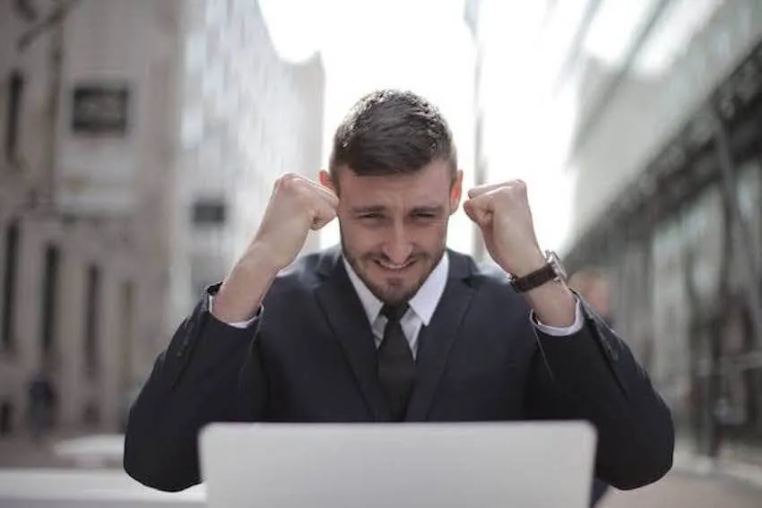 smiling man looking at his laptop with his fists up in celebration