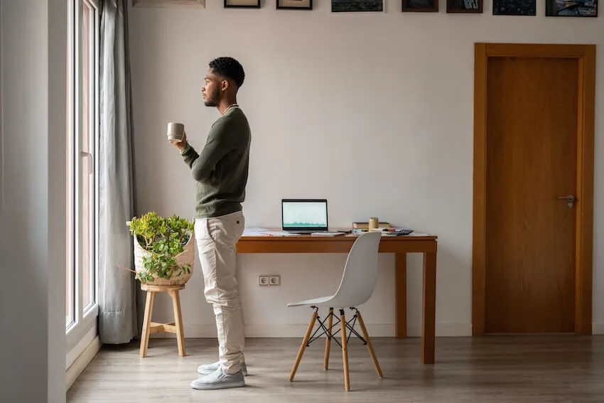 man holding a coffee mug standing in front of a window looking out