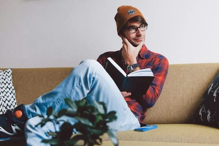 man in beanie holding a book lost in thought