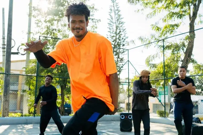 man in orange shirt smiling at the camera as he dances with his friends in the background