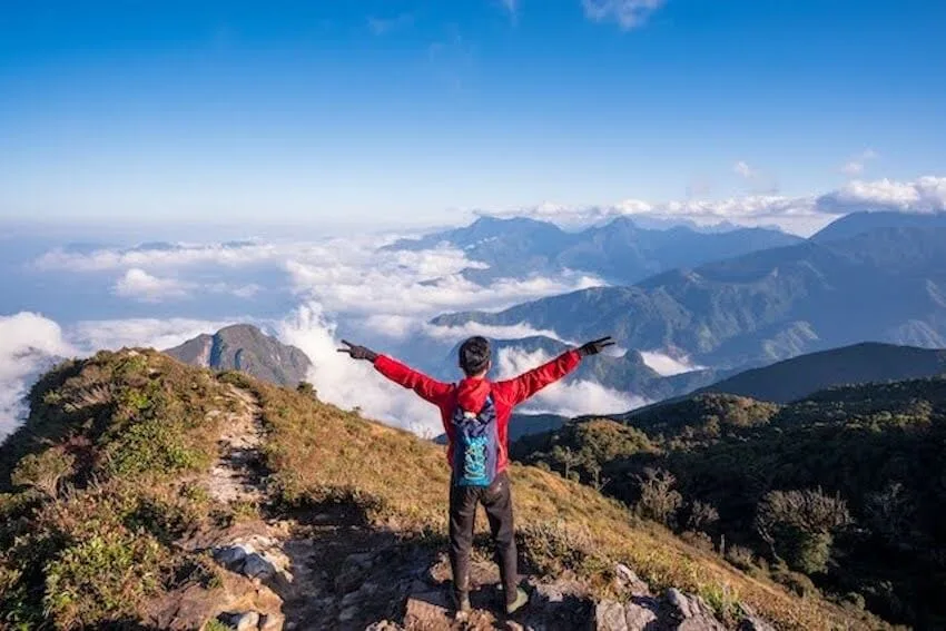 man in red jacket standing on top of a mountain with his arms out