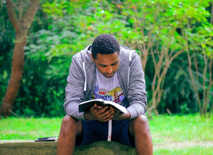 man sitting outside, reading a book